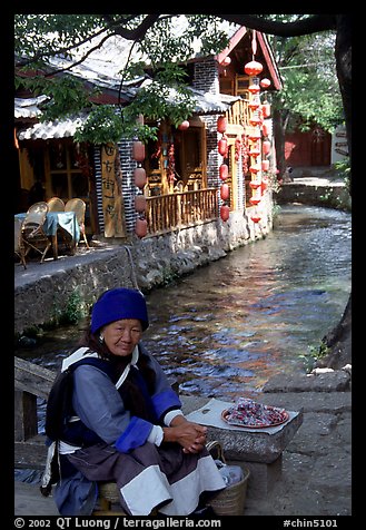 Elderly naxi woman peddles candies near a canal. Lijiang, Yunnan, China (color)