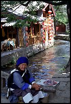 Elderly naxi woman peddles candies near a canal. Lijiang, Yunnan, China (color)