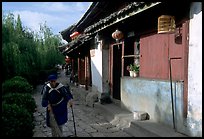 Naxi woman sweeps the floor at the door of her wooden house. Lijiang, Yunnan, China