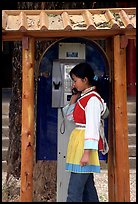 Woman in Naxi dress in a telephone booth. Lijiang, Yunnan, China (color)