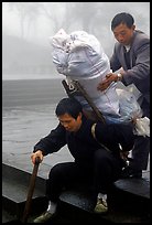 Porter getting helped to shoulder a heavy load on a back frame. Emei Shan, Sichuan, China