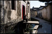 Man sitting in front of house on bridge over stream. Xidi Village, Anhui, China ( color)