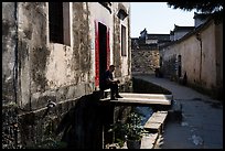 Man sitting in front of house on bridge over stream. Xidi Village, Anhui, China