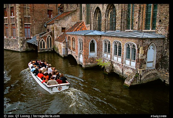 Tour boat goes by a church on a canal. Bruges, Belgium