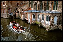 Tour boat goes by a church on a canal. Bruges, Belgium