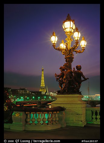 Bronze lamp post with scultpure on Pont Alexandre III, and Eiffel Tower at night. Paris, France