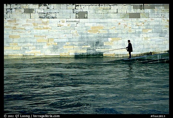 Man standing at water level fishing in the Seine River. Paris, France