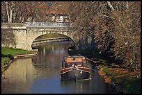 Tranquil scene with barge, bridge, and trees, Canal du Midi. Carcassonne, France