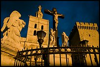 Cross with Christ, statues, and towers, evening light. Avignon, Provence, France