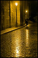 Street lamps reflected in wet pavement, with woman walking. Paris, France (color)