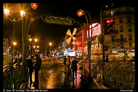 Metro entrance, boulevard, and Moulin Rouge on rainy night. Paris, France