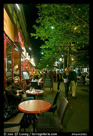 Couple walking by outdoor tables of cafe at night. Paris, France (color)