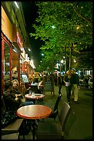 Couple walking by outdoor tables of cafe at night. Paris, France (color)