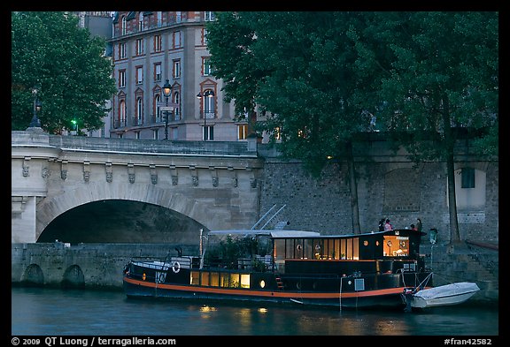 Lighted live-in barge, quay, and Pont-Neuf. Paris, France