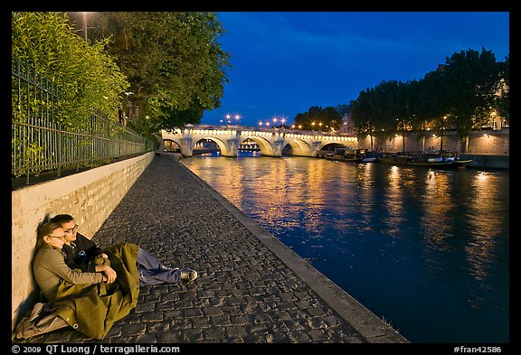 Couple sitting on quay on banks of the Seine River. Paris, France (color)