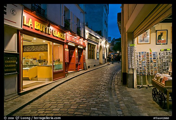 Narrow cobblestone street and businesses at night, Montmartre. Paris, France