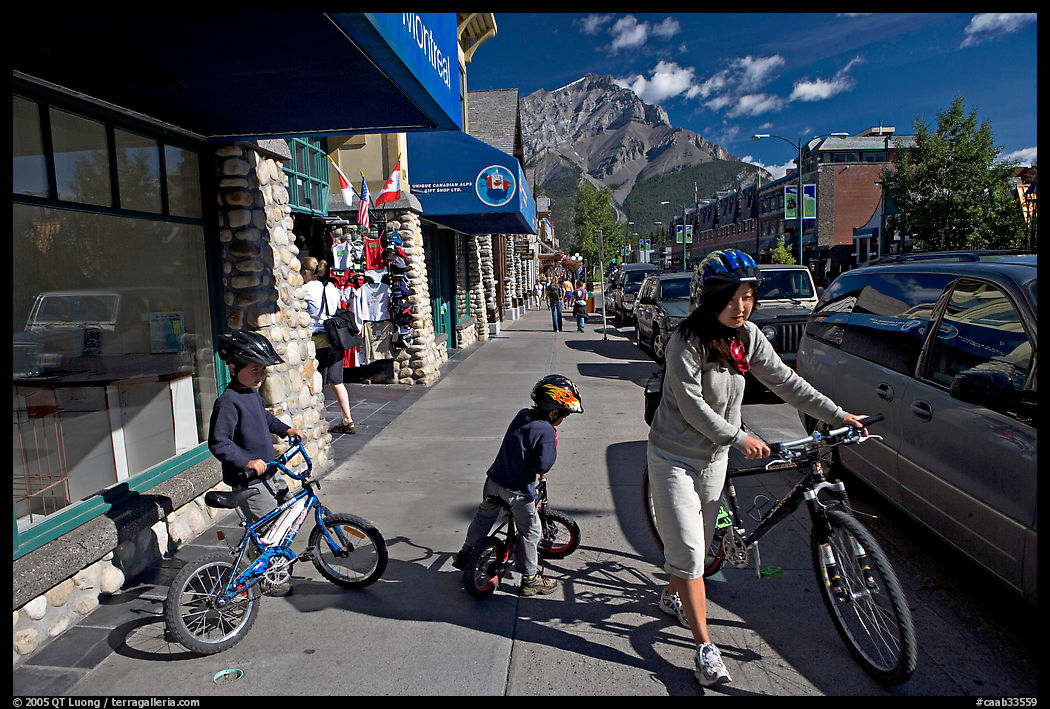 Woman and kids with mountain bikes on downtown Banff sidewalk. Banff National Park, Canadian Rockies, Alberta, Canada