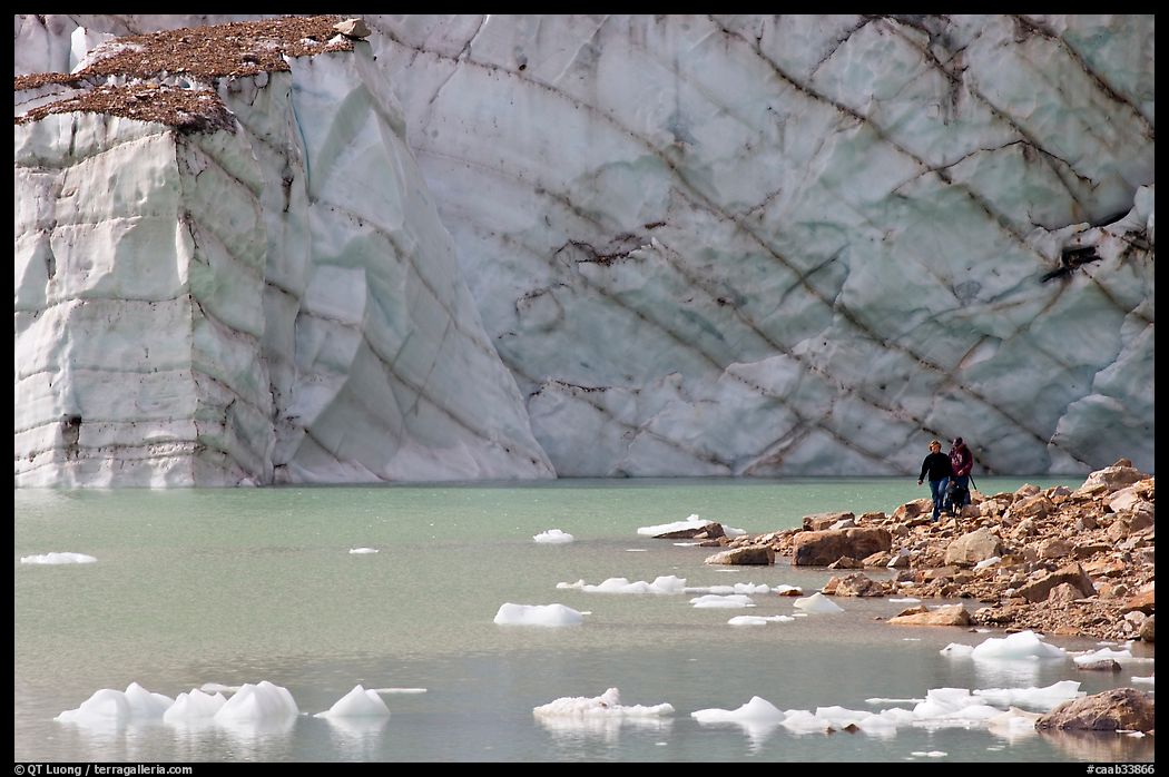 Hikers on the shore of Cavell Pond with high glacier wall behind. Jasper National Park, Canadian Rockies, Alberta, Canada