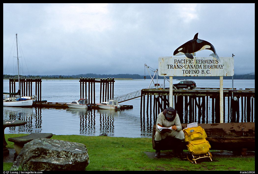 Backpacker sitting under the Transcanadian terminus sign, Tofino. Vancouver Island, British Columbia, Canada