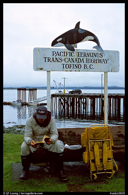 Backpacker sitting under the Transcanadian terminus sign, Tofino. Vancouver Island, British Columbia, Canada