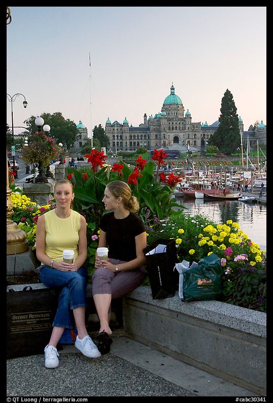 Women with shopping bags and coffee cups at the Inner Harbour, sunset. Victoria, British Columbia, Canada