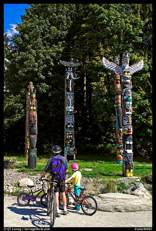 Family with bicycles looking at Totems, Stanley Park. Vancouver, British Columbia, Canada