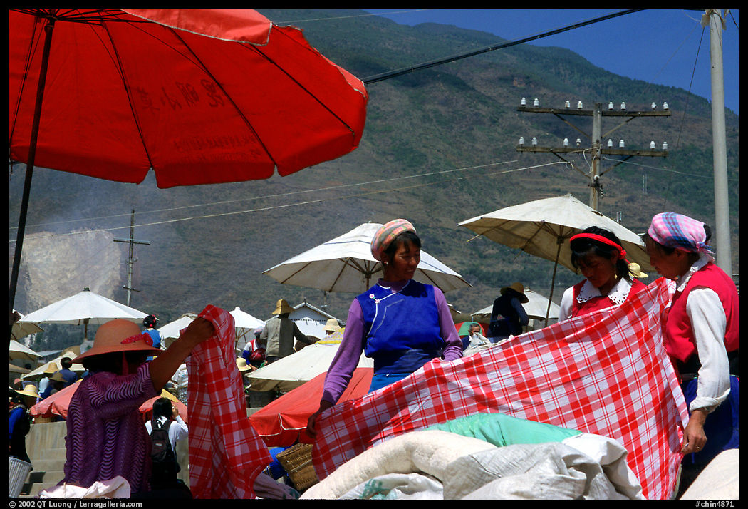 Bai women examining a piece of cloth at the Monday market. Shaping, Yunnan, China
