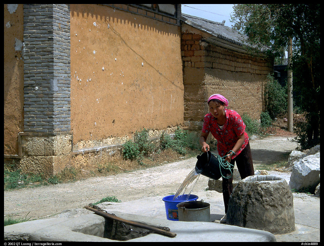 Bai woman fills up a water bucket at the well. Shaping, Yunnan, China