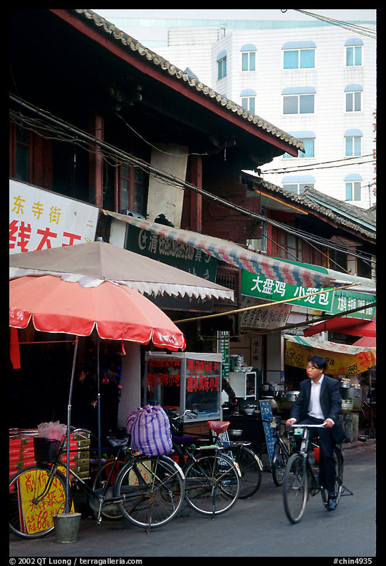 Man on bicycle in front of wooden buildings. Kunming, Yunnan, China