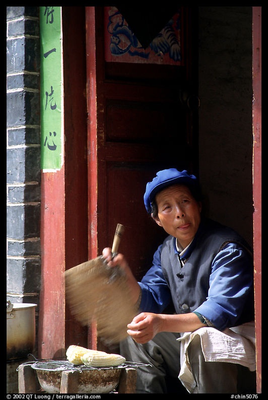 Naxi woman at doorway selling broiled corn. Lijiang, Yunnan, China