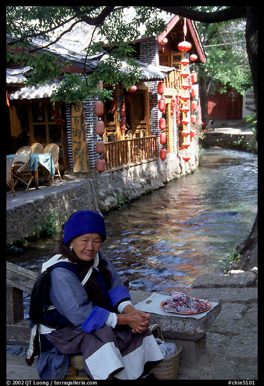 Elderly naxi woman peddles candies near a canal. Lijiang, Yunnan, China
