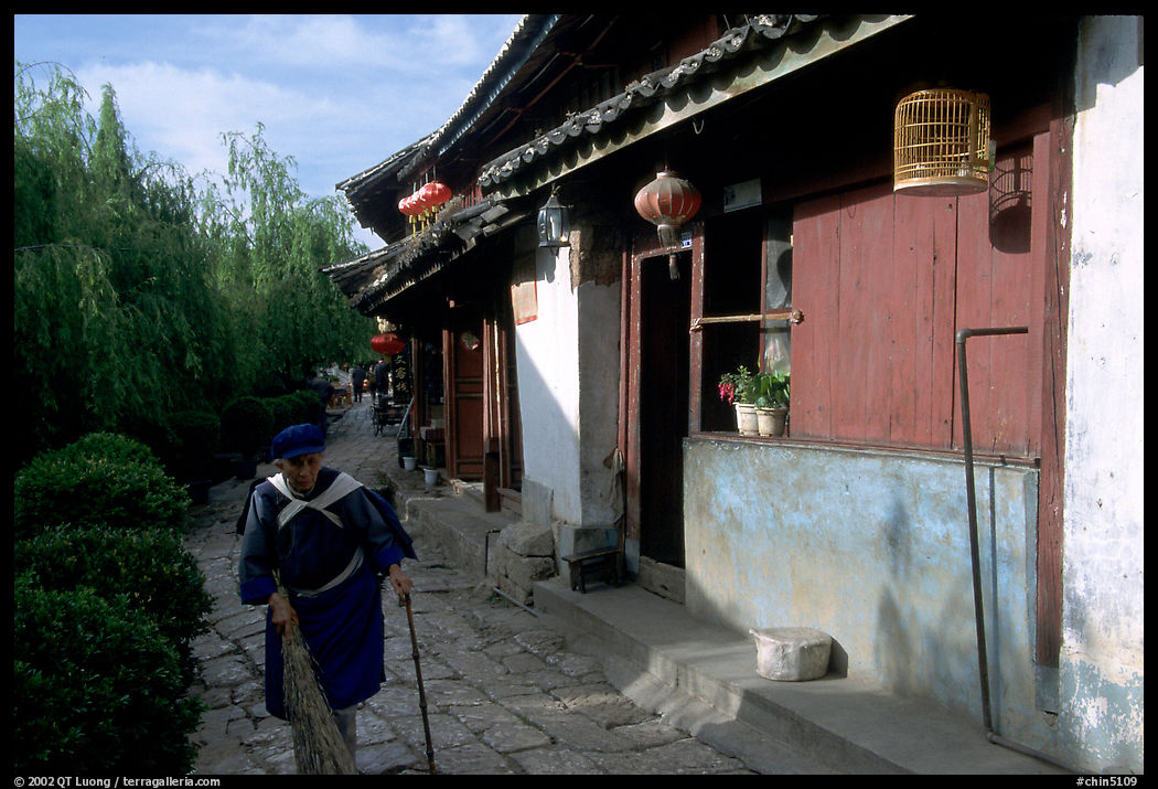 Naxi woman sweeps the floor at the door of her wooden house. Lijiang, Yunnan, China
