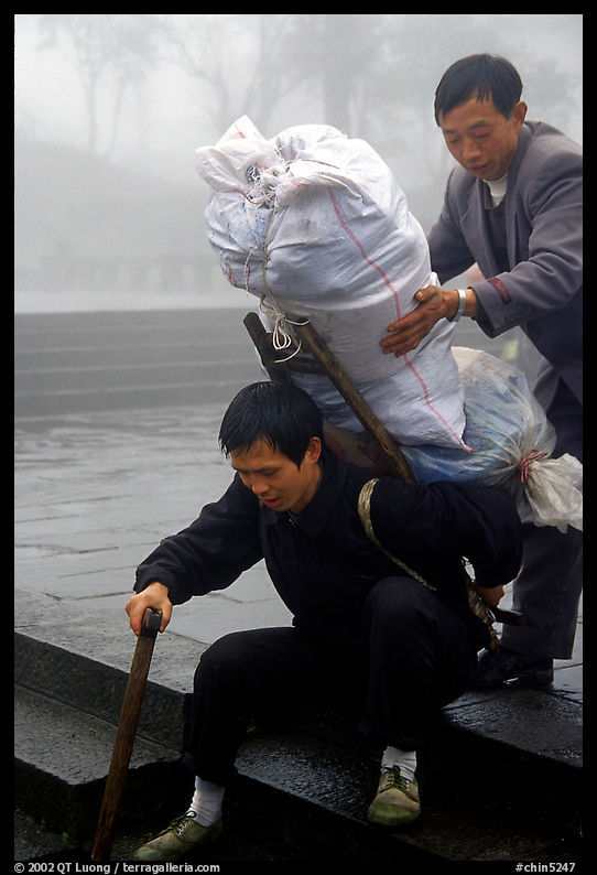 Porter getting helped to shoulder a heavy load on a back frame. Emei Shan, Sichuan, China