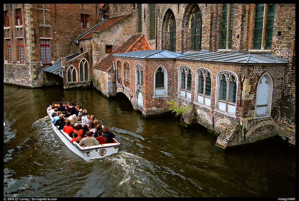Tour boat goes by a church on a canal. Bruges, Belgium