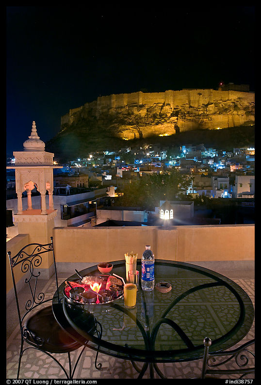 Rooftop restaurant table with food served and view of Mehrangarh Fort by night. Jodhpur, Rajasthan, India