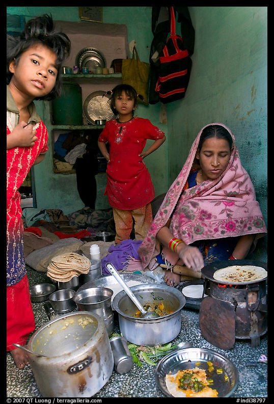 Woman cooking, flanked by two girls. Jodhpur, Rajasthan, India
