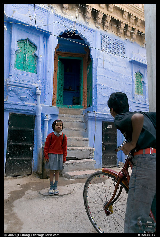 Boy on bicycle looking at girl in front of blue house. Jodhpur, Rajasthan, India