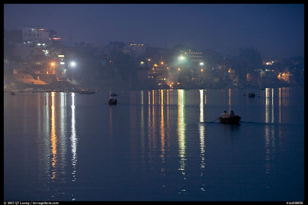 Rowboats and reflected lights on the Ganges River at dusk. Varanasi, Uttar Pradesh, India
