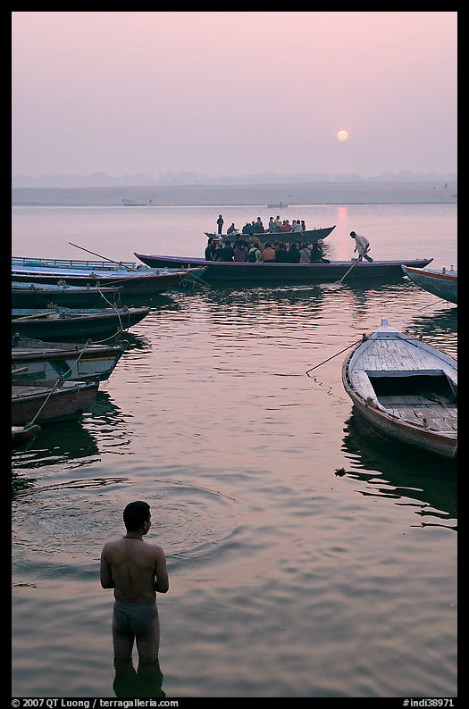 Man standing in Ganga River and boats at sunrise. Varanasi, Uttar Pradesh, India