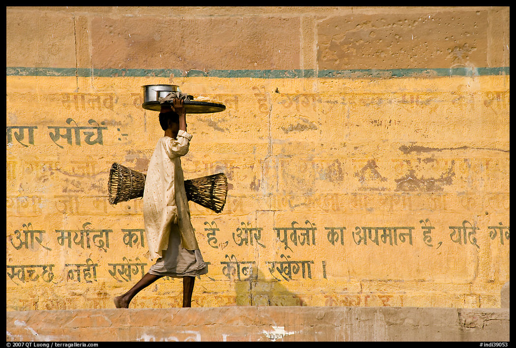 Man carrying a plater in front of wall with inscriptions in Hindi. Varanasi, Uttar Pradesh, India