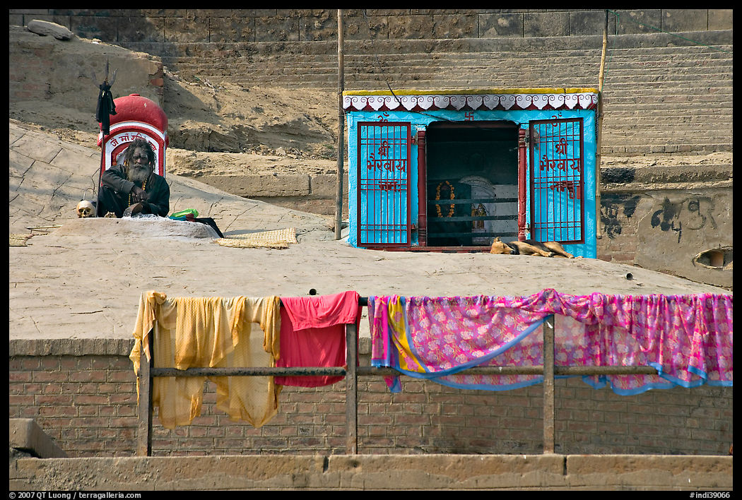 Sadhu sitting next to shrine and laundry. Varanasi, Uttar Pradesh, India