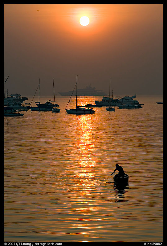 Man fishing from rowboat and anchored yachts, sunrise. Mumbai, Maharashtra, India