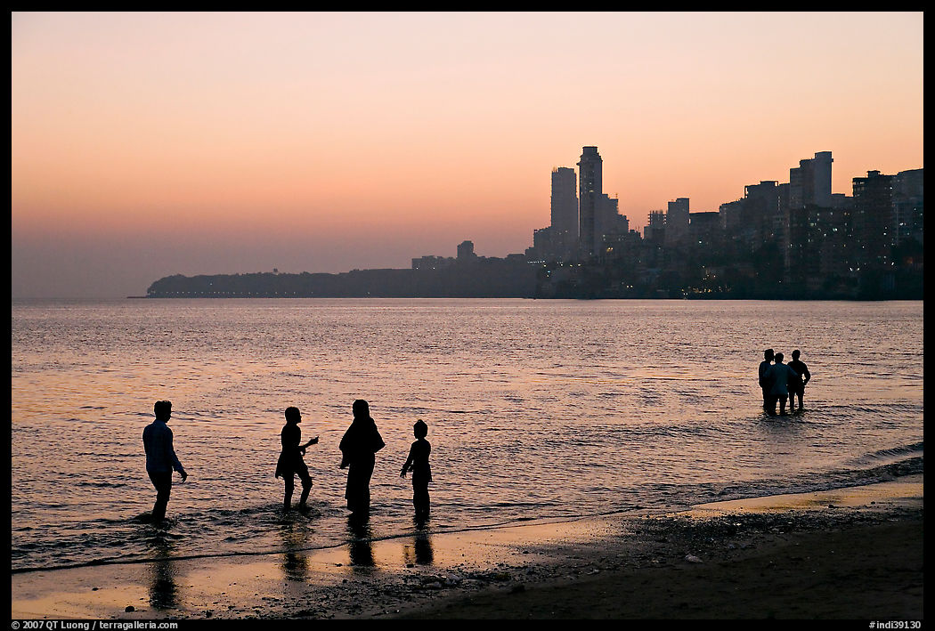 People standing in water at sunset with skyline behind, Chowpatty Beach. Mumbai, Maharashtra, India