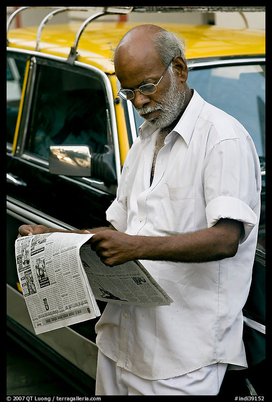 Man reading newspaper next to taxi. Mumbai, Maharashtra, India