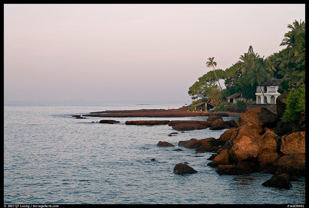 Boulders, beachfront house, and palm trees at sunrise. Goa, India