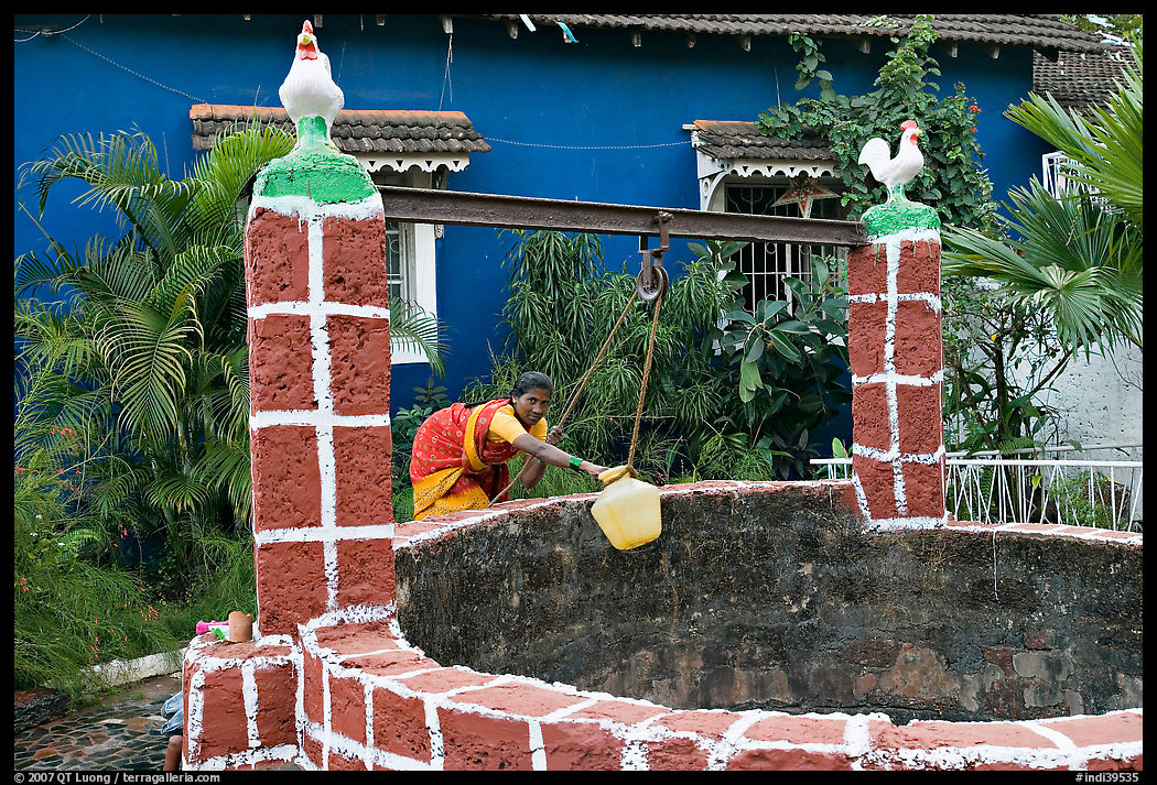 Woman retrieving water from well with blue house behind, Panjim. Goa, India