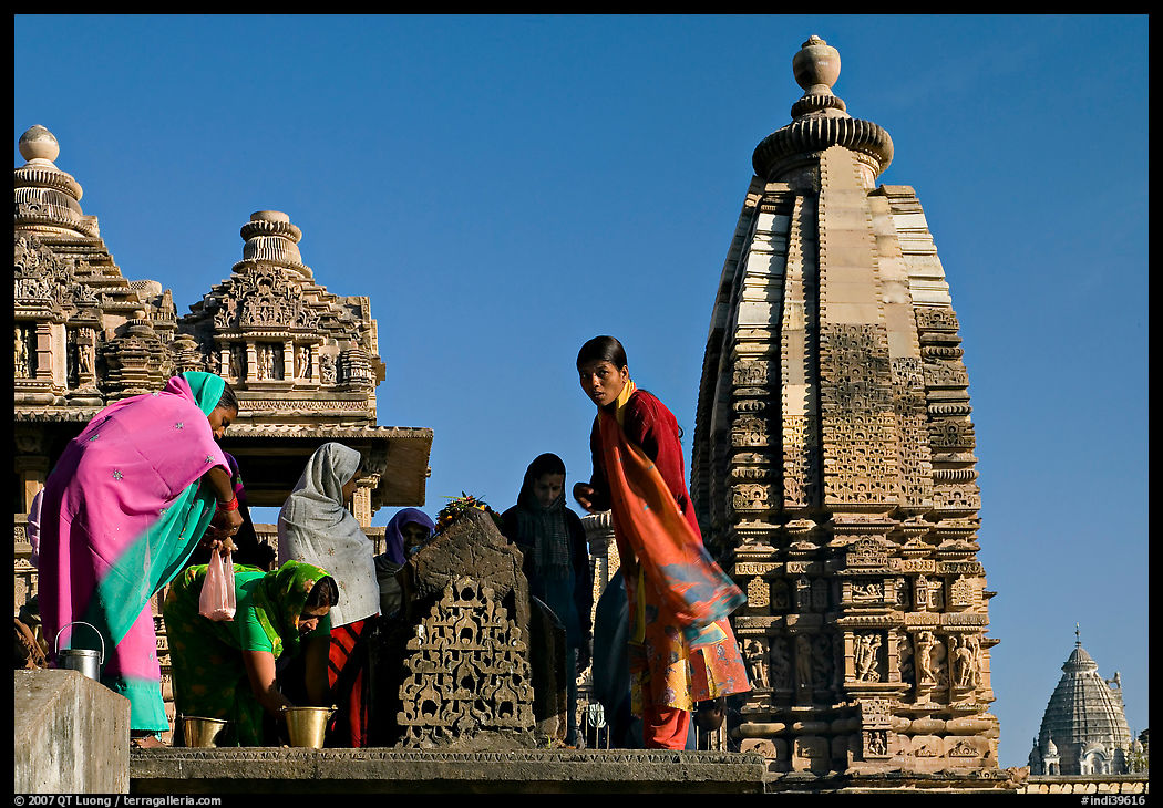 Women worshipping image with of Vahara and Lakshmana temples behind. Khajuraho, Madhya Pradesh, India