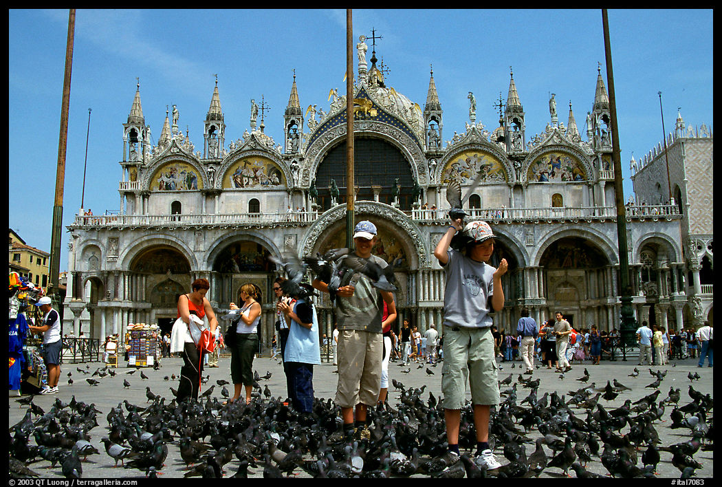 Children feeding a flock of pigeon, in front of the Basilica San Marco, mid-day. Venice, Italy