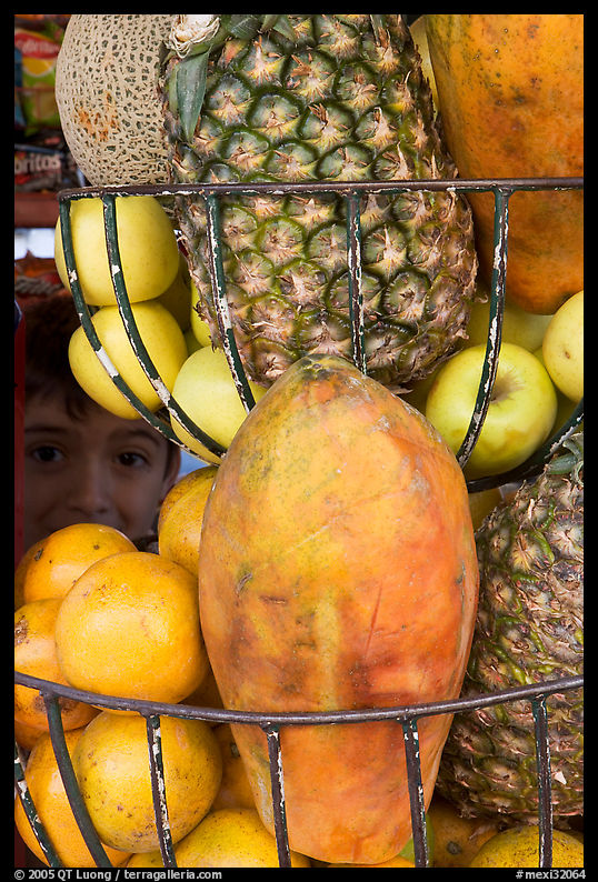 Boy peers from behind fruits offered at a juice stand, Tlaquepaque. Jalisco, Mexico