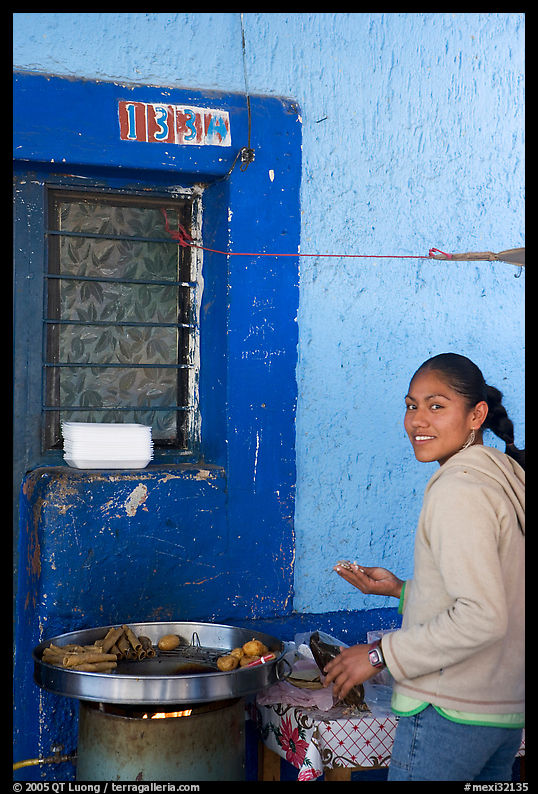 Woman preparing food outside a blue wall, Tonala. Jalisco, Mexico